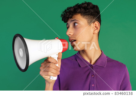 Cropped portrait of young boy in purple T-shirt speaking into megaphone isolated over green background. Giving information Cropped portrait of young boy in purple T-shirt speaking into megaphone isolated over green background. Giving information 83460138