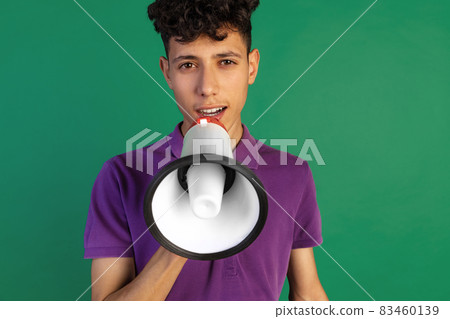 Cropped portrait of young boy in purple T-shirt speaking into megaphone isolated over green background Cropped portrait of young boy in purple T-shirt speaking into megaphone isolated over green background 83460139