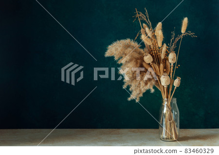 Bouquet of beige dried flowers in a glass vase on green-blue background. 83460329