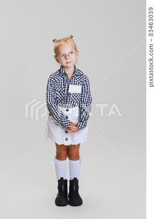 Full-length portrait of little cute girl, child in glasses and checkered shirt isolated over gray background Full-length portrait of little cute girl, child in glasses and checkered shirt isolated over gray background 83463039