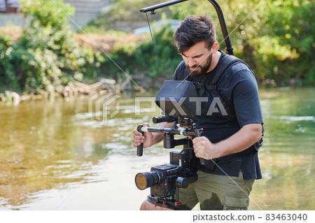 a professionally equipped cameraman shoots in the water surrounded by beautiful nature. a professionally equipped cameraman shoots in the water surrounded by beautiful nature. 83463040