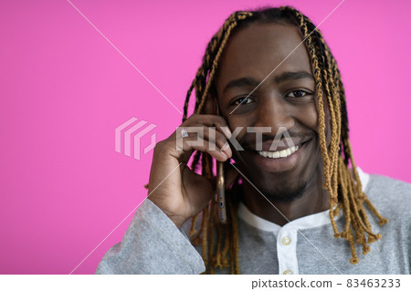 afro guy uses a phone while posing in front of a pink background. afro guy uses a phone while posing in front of a pink background. 83463233