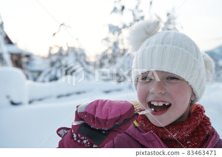cute little girl while eating icicle on beautiful winter day cute little girl while eating icicle on beautiful winter day 83463471