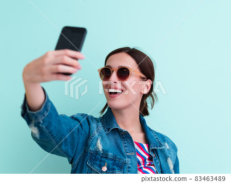 Portrait of young girl taking selfie on blue background 83463489