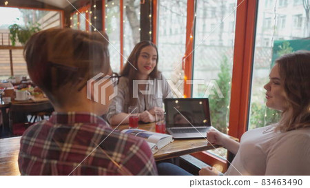 Three students guy and girls having discussion while study sitting in a cafe with lights running on the background as they sit at a table with different books on it. 4K footage Three students guy and girls having discussion while study sitting in a cafe with lights running on the background as they sit at a table with different books on it. 4K footage 83463490
