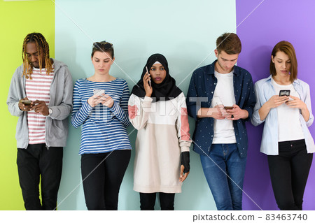 diverse teenagers use mobile devices while posing for a studio photo in front of a pink background diverse teenagers use mobile devices while posing for a studio photo in front of a pink background 83463740