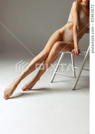 Cropped shot of young beautiful pretty woman in light underwear sitting on high chair isolated over gray studio background. 83463872