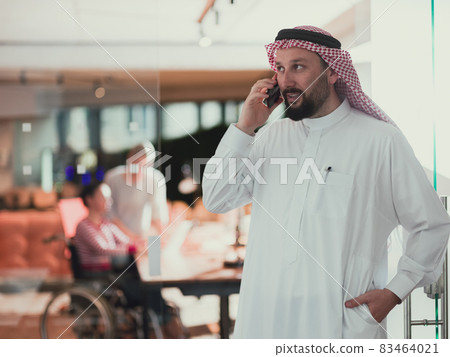 Middle eastern Arab businessman in the office speaking on smartphone in front of his team Middle eastern Arab businessman in the office speaking on smartphone in front of his team 83464021