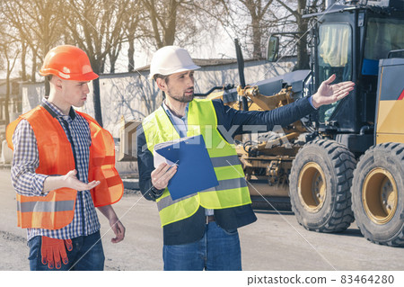 Two construction engineers inspect the construction site and discuss the implementation of the plans. Surveyor and equipment at construction site. Two construction engineers inspect the construction site and discuss the implementation of the plans. Surveyor and equipment at construction site. 83464280