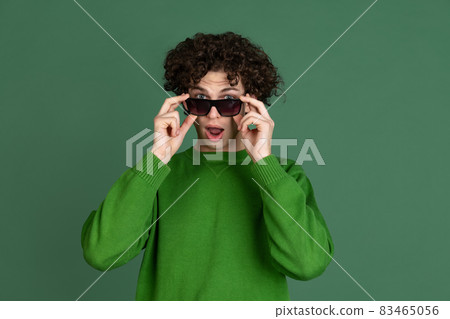 Cropped portrait of young man in green sweater and stylish sunglasses isolated over dark green background. Fashionable youth Cropped portrait of young man in green sweater and stylish sunglasses isolated over dark green background. Fashionable youth 83465056