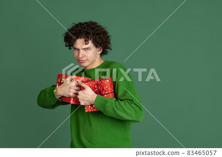 Cropped portrait of young man in green sweater with gift box isolated over dark green background. New Year celebration Cropped portrait of young man in green sweater with gift box isolated over dark green background. New Year celebration 83465057