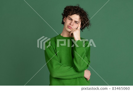 Cropped portrait of young man in green sweater with thinking facial expression isolated over dark green background Cropped portrait of young man in green sweater with thinking facial expression isolated over dark green background 83465060