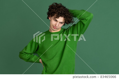 Cropped portrait of young man in green sweater with facial expression of misunderstanding isolated over dark green background Cropped portrait of young man in green sweater with facial expression of misunderstanding isolated over dark green background 83465066