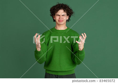 Cropped portrait of young man in green sweater with irritated facial expression of misunderstanding isolated over dark green background Cropped portrait of young man in green sweater with irritated facial expression of misunderstanding isolated over dark green background 83465072