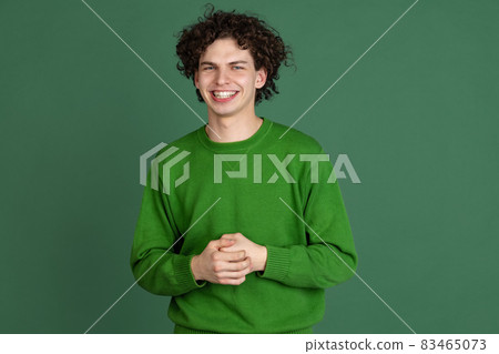 Cropped portrait of young man in green sweater smiling isolated over dark green background Cropped portrait of young man in green sweater smiling isolated over dark green background 83465073