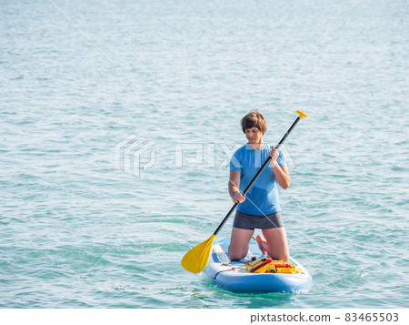 Handsome paddle boarder. Sportsman on knees paddling on stand up paddleboard. SUP surfing. Active lifestyle. Outdoor recreation. Vacation on seaside. Handsome paddle boarder. Sportsman on knees paddling on stand up paddleboard. SUP surfing. Active lifestyle. Outdoor recreation. Vacation on seaside. 83465503