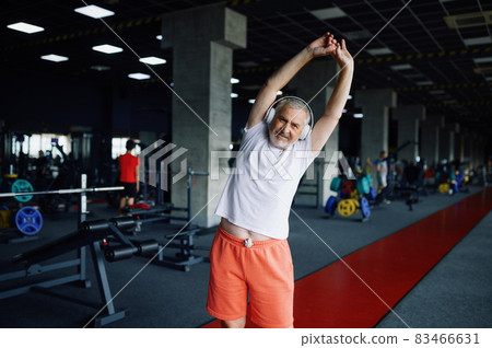 Old man in headphones doing fit exercise, gym 83466631