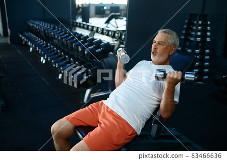Elderly man, workout with dumbbells on bench, gym Elderly man, workout with dumbbells on bench, gym 83466636