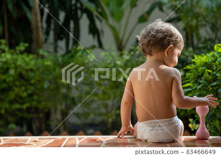 a charming toddler sits on the steps of a house in the sunlight. back view. a charming toddler sits on the steps of a house in the sunlight. back view. 83466649