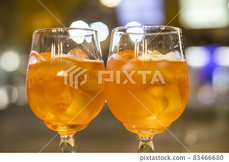Two glasses of wine with orange coctail stand on a wooden table in a cafe.Italian alcoholic drink with oranges and ice. Close-up, selective focus Two glasses of wine with orange coctail stand on a wooden table in a cafe.Italian alcoholic drink with oranges and ice. Close-up, selective focus 83466680