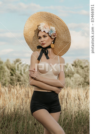 Girls in tops and shorts, in a hat and with a rim of flowers, posing against the background of nature. The first girl holds the stems of the reed. Another girl with a basket in which different flowers 83466951