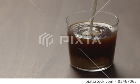 pour cream in coffee in tumbler glass on walnut wood table with copy space 83467063