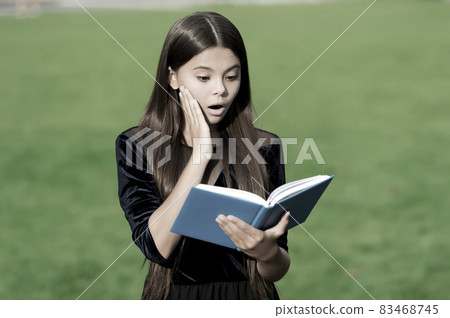 Learn to discover. Surprised child read book outdoors. 83468745