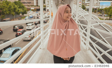 Smiling girl in hijab goes behind the camera on the transition over road traffic. Jakarta. Indonesia. Smiling girl in hijab goes behind the camera on the transition over road traffic. Jakarta. Indonesia. 83468946