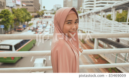 A smiling Muslim girl is walking on the transition over road traffic. Indonesia. 83469009