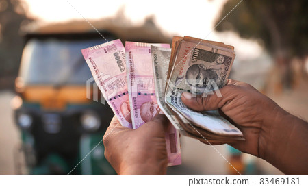 A man recounts Indian rupee money amid tuk tuk. 83469181