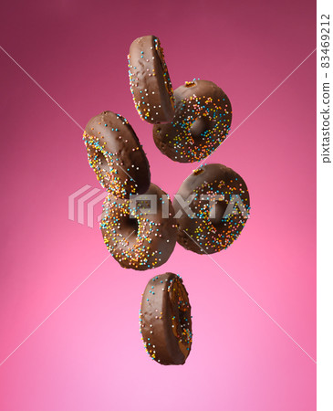 chocolate round donuts with multicolored sugar sprinkles levitate on a pink background chocolate round donuts with multicolored sugar sprinkles levitate on a pink background 83469212