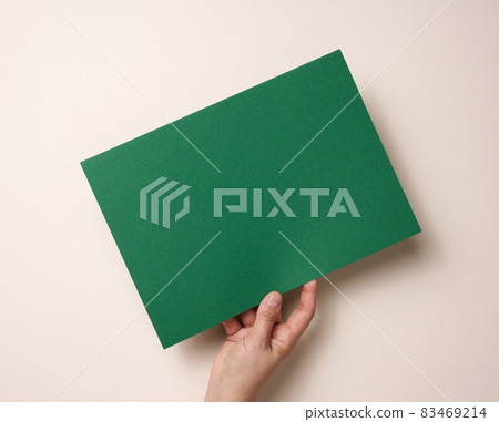 Female hand holding empty green paper on a beige background. Copy space Female hand holding empty green paper on a beige background. Copy space 83469214