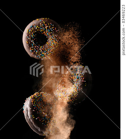 chocolate round donuts with multicolored sugar sprinkles levitate in a cloud of brown cocoa on a black background chocolate round donuts with multicolored sugar sprinkles levitate in a cloud of brown cocoa on a black background 83469223