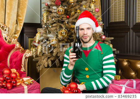 Man in santa hat with champagne bottle at Christmas tree 83469235