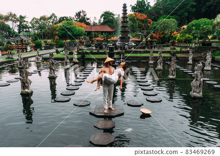A beautiful couple is traveling on the island of Bali in Indonesia. A couple walks through a water temple in Indonesia. Travel to Asia. The tourists travel. The man lifted the woman in his arms 83469269