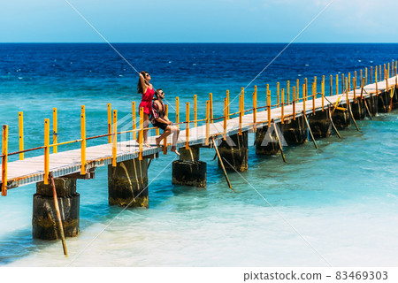 Happy couple on vacation strolling along a wooden pier above the tropical blue ocean. Beautiful couple on the coast in Indonesia. A couple in love is resting on the sea. Honeymoon trip. Copy space 83469303