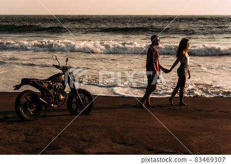 A man and a woman meet the sunset on the island of Bali. A couple in love on the beach meets the sunset. Beautiful couple on a bike. Lovers on the beach. Silhouette of loving couple on sea. Copy space A man and a woman meet the sunset on the island of Bali. A couple in love on the beach meets the sunset. Beautiful couple on a bike. Lovers on the beach. Silhouette of loving couple on sea. Copy space 83469307