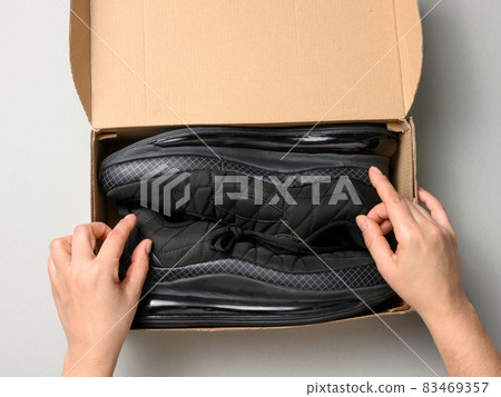 female hands are holding a brown cardboard box with black sports sneakers on a gray table, inspecting an online order 83469357
