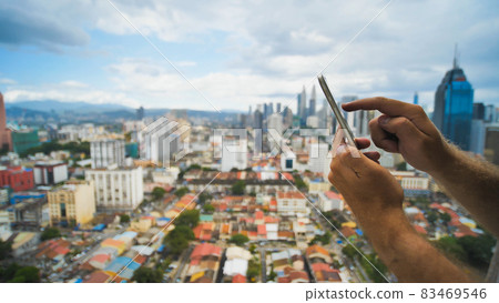 The guy is working with a smartphone on a blurred background. Kuala Lumpur. Hands and phone close up. Malaysia. 83469546