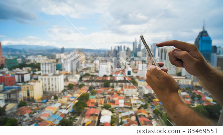The guy is working with a smartphone on a blurred background. Kuala Lumpur. Hands and phone close up. Malaysia. 83469551
