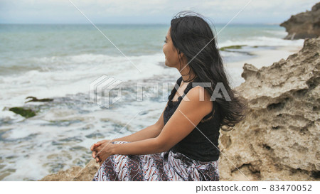 Young smiling indonesian girl poses on a stony beach background. Slow Motion. 83470052