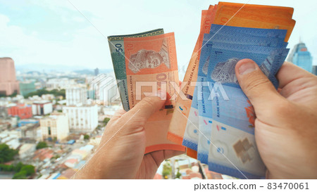 A young man recounts in his hands the money of Malaysia against the background of the city center of Kuala Lumpur. A young man recounts in his hands the money of Malaysia against the background of the city center of Kuala Lumpur. 83470061