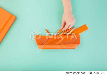 Child's hand keeping all the pencils, pens, scissors, etc. in orange pencil case. Back to school Child's hand keeping all the pencils, pens, scissors, etc. in orange pencil case. Back to school 83470178