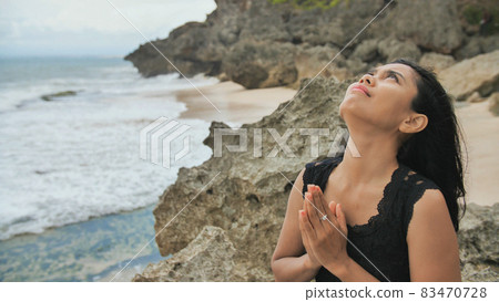 Indonesian girl praying on a rocky Bali beach. Indonesian girl praying on a rocky Bali beach. 83470728