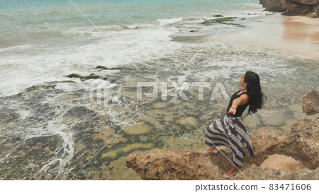 Indonesian girl enjoys life with outstretched hands on the rocky shore on the island of Bali. 83471606