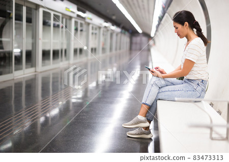Oriental woman with smartphone sitting on bench in subway station Oriental woman with smartphone sitting on bench in subway station 83473313
