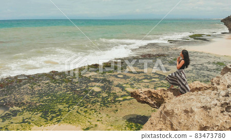 Indonesian girl praying on a rocky Bali beach. Indonesian girl praying on a rocky Bali beach. 83473780
