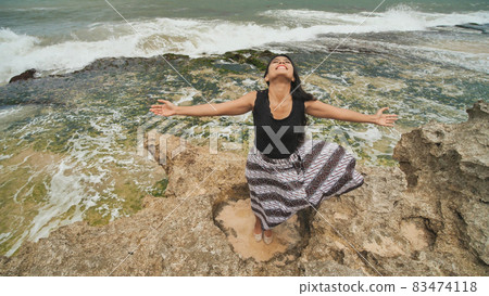Indonesian girl enjoys life with outstretched hands on the rocky shore on the island of Bali. Indonesian girl enjoys life with outstretched hands on the rocky shore on the island of Bali. 83474118