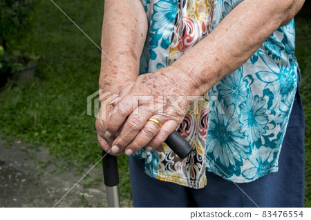 Elderly hand holding a walking cane , Asian old woman standing with hands on a walking stick Elderly hand holding a walking cane , Asian old woman standing with hands on a walking stick 83476554