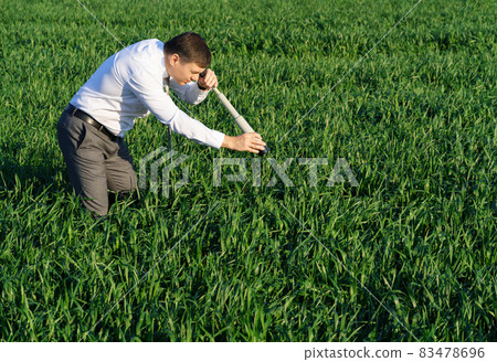 businessman poses with a spyglass, he looks into the grass and looks for something, green grass and blue sky as background businessman poses with a spyglass, he looks into the grass and looks for something, green grass and blue sky as background 83478696